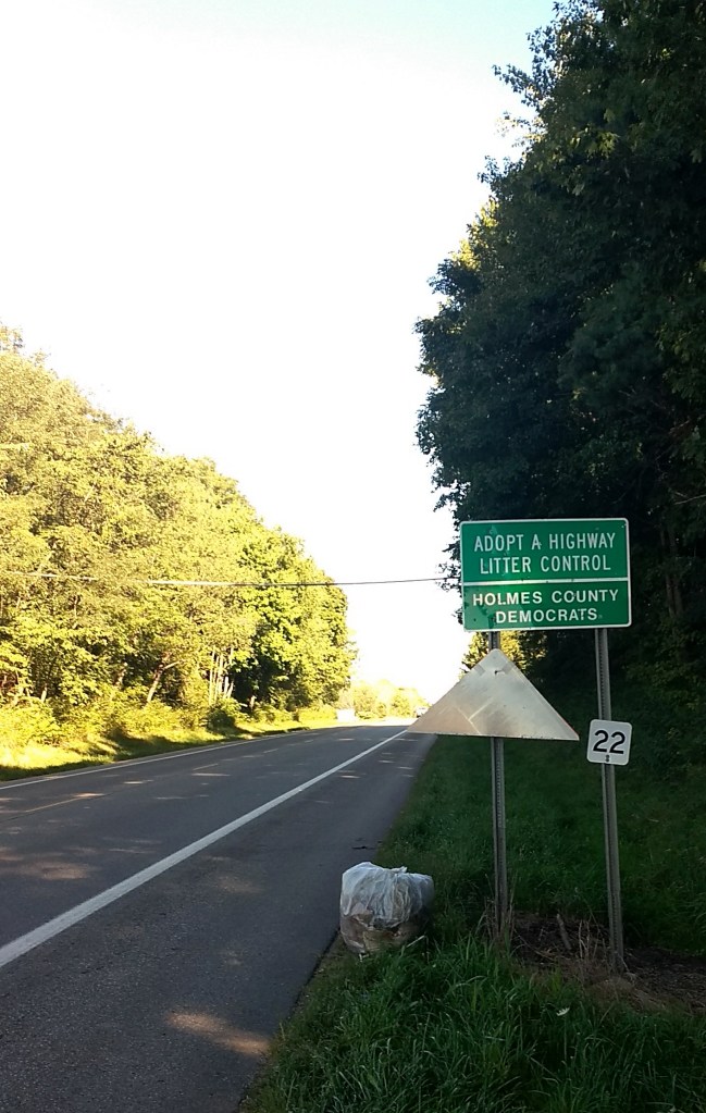 A road in Holmes County with a sign in the shoulder that reads Adopt a Highway Litter Control - Holmes County Democrats.